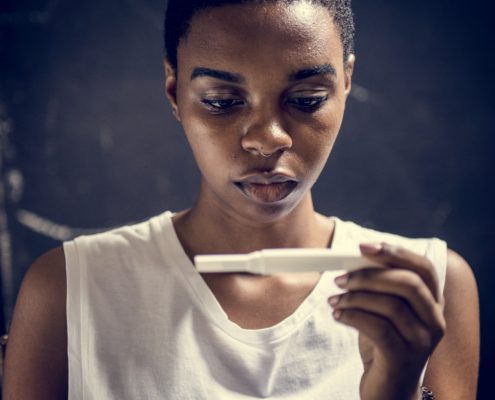 Nahaufnahme einer jungen Frau, die mit ernstem Gesicht auf einen Schwangerschaftstest schaut.