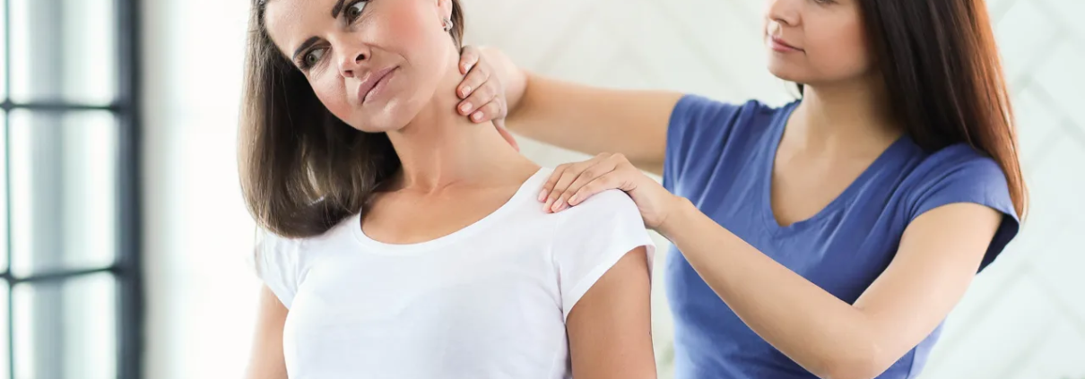 Eine Physiotherapeutin massiert eine andere Frau im Nacken.